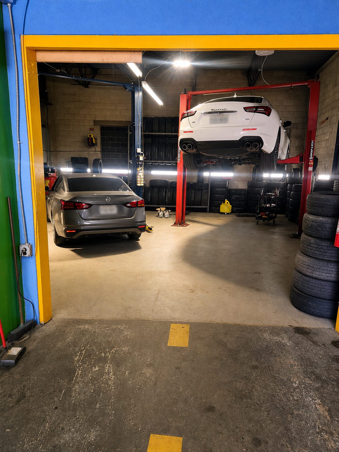 Inside Mad Dawgz Tire & Auto Repair — a Maserati on the lift and a Nissan in the bay, surrounded by stocked tire racks